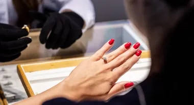 Dłoń z czerwonym manicurem i pierścionkiem oglądana przez jubilera w czarnych rękawiczkach